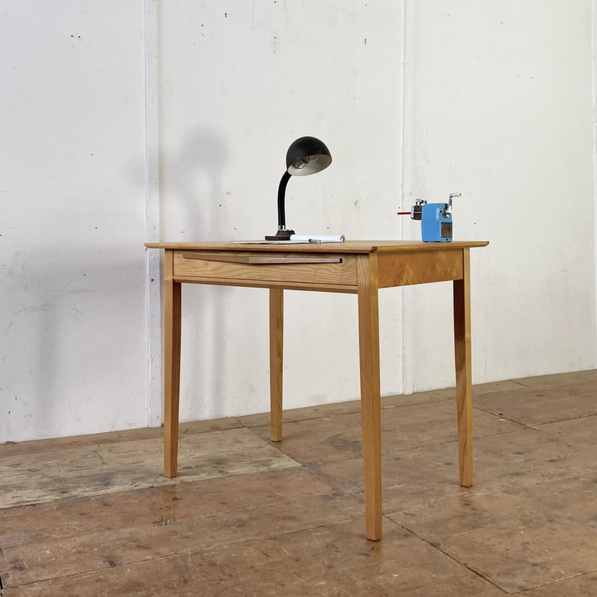 Deuxieme.shop 60er 70er Jahre Schreibtisch. Schlichter Eschenholz Schreibtisch mit Schublade. Das Tischblatt ist furniert, die leicht konischen Tischbeine und die Schublade sind aus Vollholz. Der Tisch ist in stabilem Zustand mit leichten Gebrauchsspuren. 